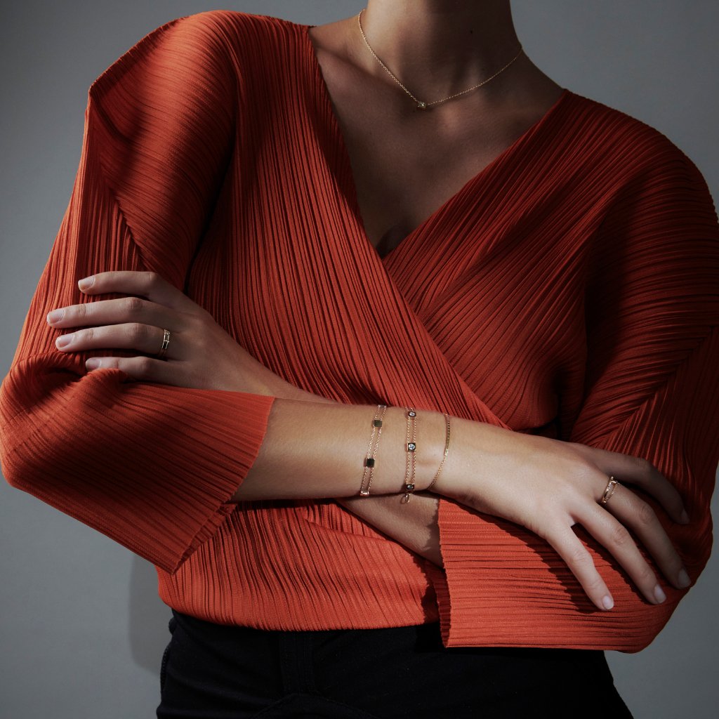 Torso of woman in orange top wearing bliss lau necklace and bracelets